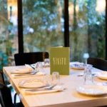 Table set with vintage plates and a green Rikito menu by a garden window at Rikito Palma