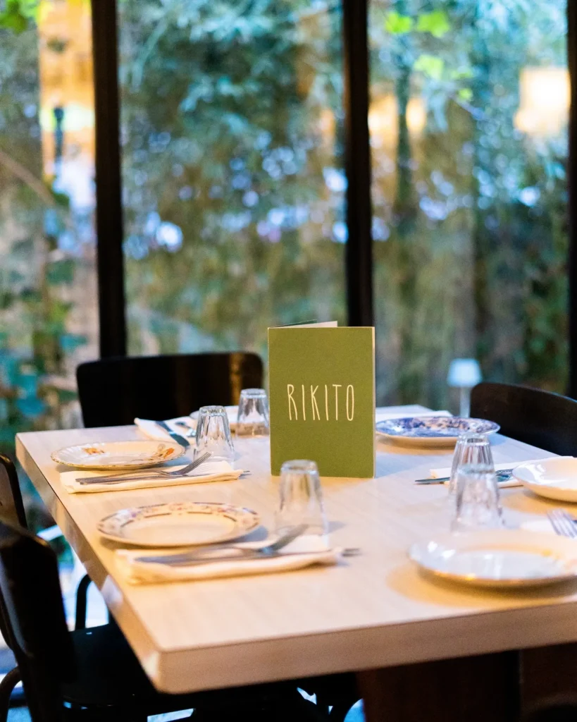 Table set with vintage plates and a green Rikito menu by a garden window at Rikito Palma