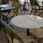 Green-and-cream rattan bistro chairs around marble tables on the terrace at Rikito Palma