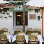 White-clothed terrace tables and bistro chairs around a tree beneath the Rikito neon sign at Rikito Palma