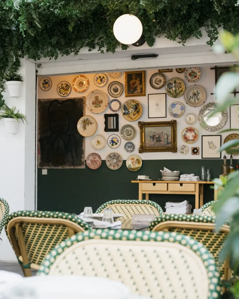 Terrace seating beneath a wall of vintage decorative plates and ivy at Rikito Palma