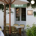 Terrace tables and green rattan bistro chairs under a parasol by the Rikito neon sign at Rikito Palma