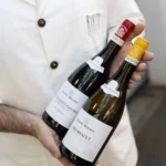 Staff member in a Rikito jacket holding bottles of Burgundy wine at Rikito Palma