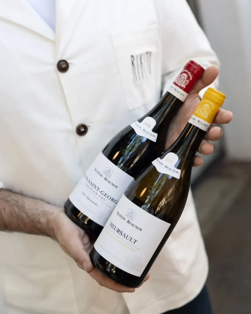 Staff member in a Rikito jacket holding bottles of Burgundy wine at Rikito Palma