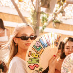 Woman holding a colorful Shellona Saint-Tropez fan at the beach club