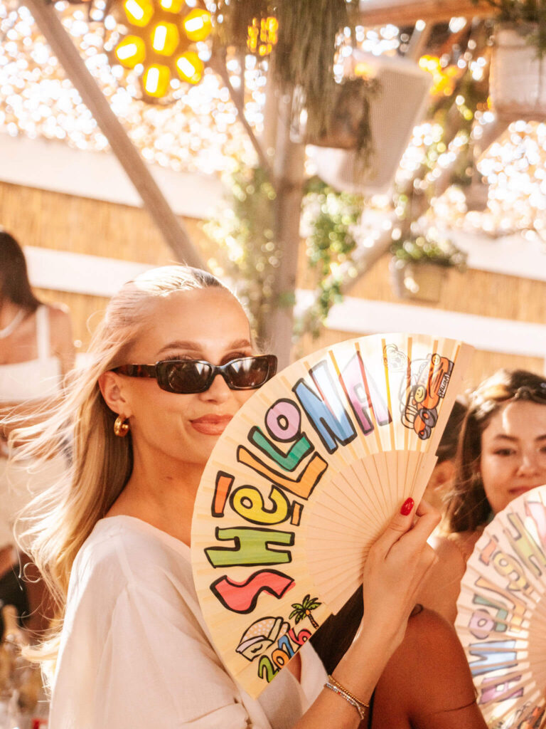 Woman holding a colorful Shellona Saint-Tropez fan at the beach club