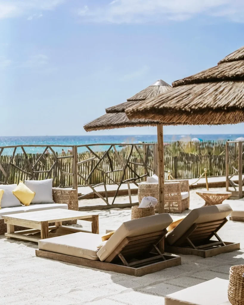 Beachfront lounge with sofas and sunbeds under a thatched umbrella and sea view at Shellona Saint-Tropez