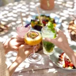 Guests toasting with cocktails over salads on a dappled table at Shellona Saint-Tropez