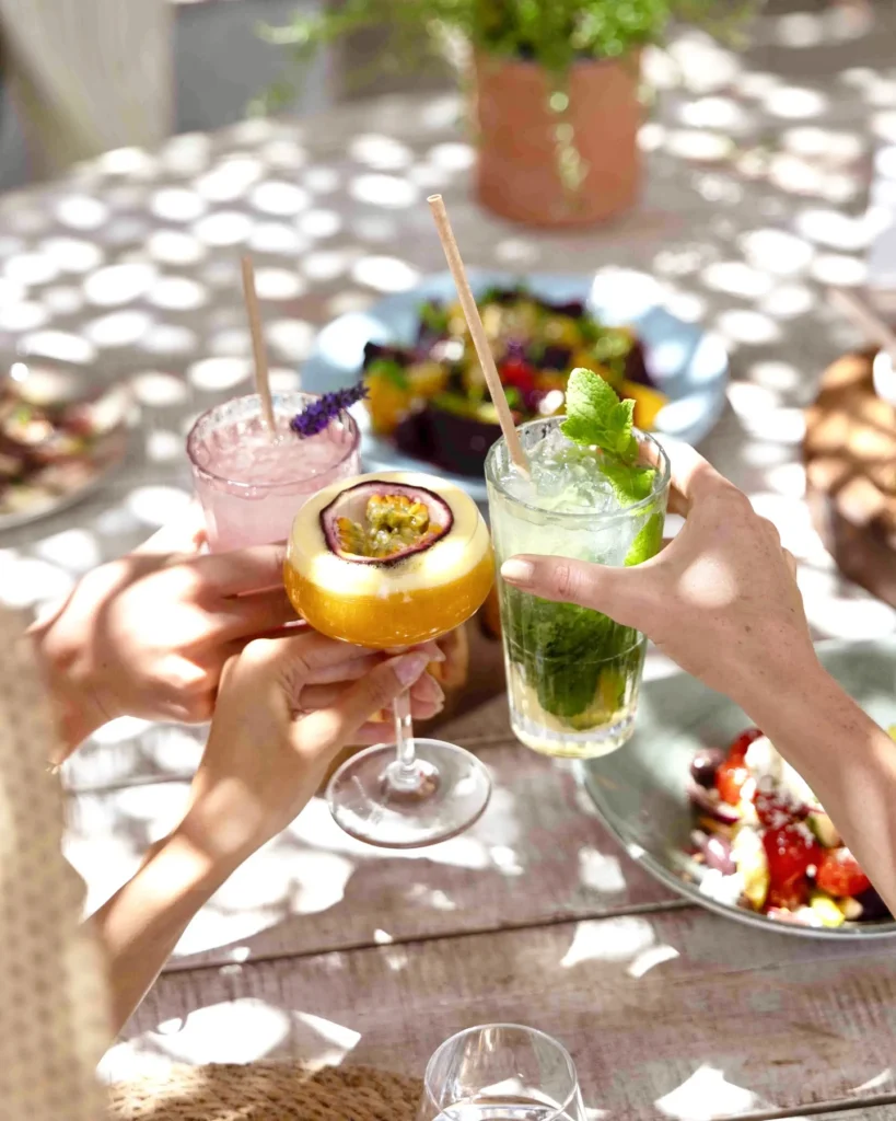 Guests toasting with cocktails over salads on a dappled table at Shellona Saint-Tropez