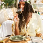 Guest in a printed headscarf sipping white wine at a sunny table at Shellona Saint-Tropez