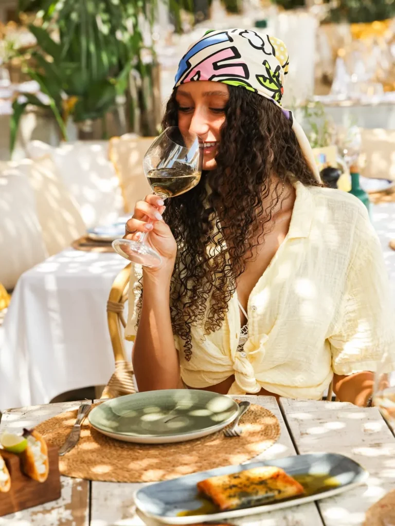 Guest in a printed headscarf sipping white wine at a sunny table at Shellona Saint-Tropez