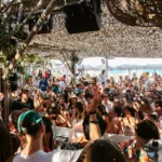Dense party crowd beneath the woven canopy with the sea beyond at Shellona Saint-Tropez