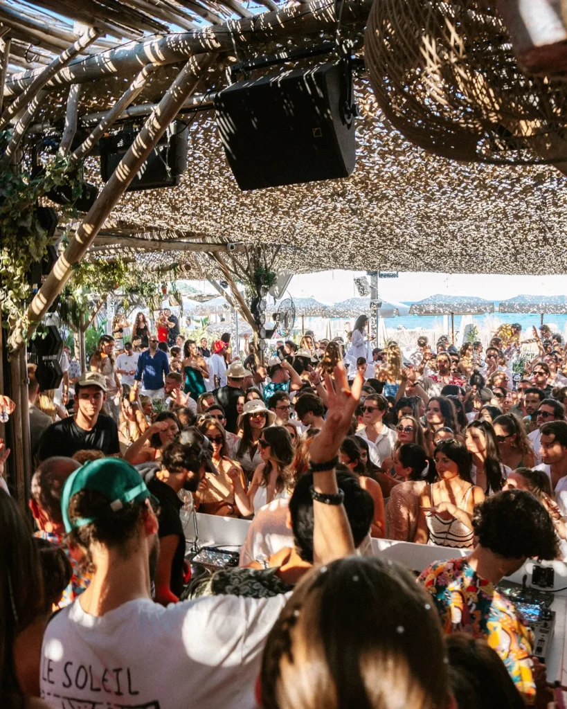 Dense party crowd beneath the woven canopy with the sea beyond at Shellona Saint-Tropez