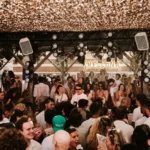 Packed crowd dancing beneath the lit Shellona sign and stage lights at Shellona Saint-Tropez