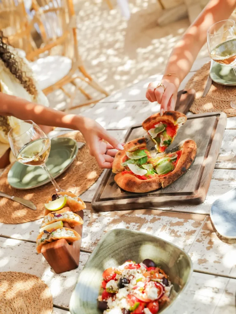Pizza, tacos and Greek salad shared with white wine on a rustic table at Shellona Saint-Tropez