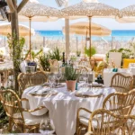 Rattan-chaired tables under parasols framed by greenery at Shellona Saint-Tropez