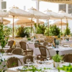 Rattan sofas and pink loungers with a fringed umbrella overlooking the sea at Shellona Saint-Tropez