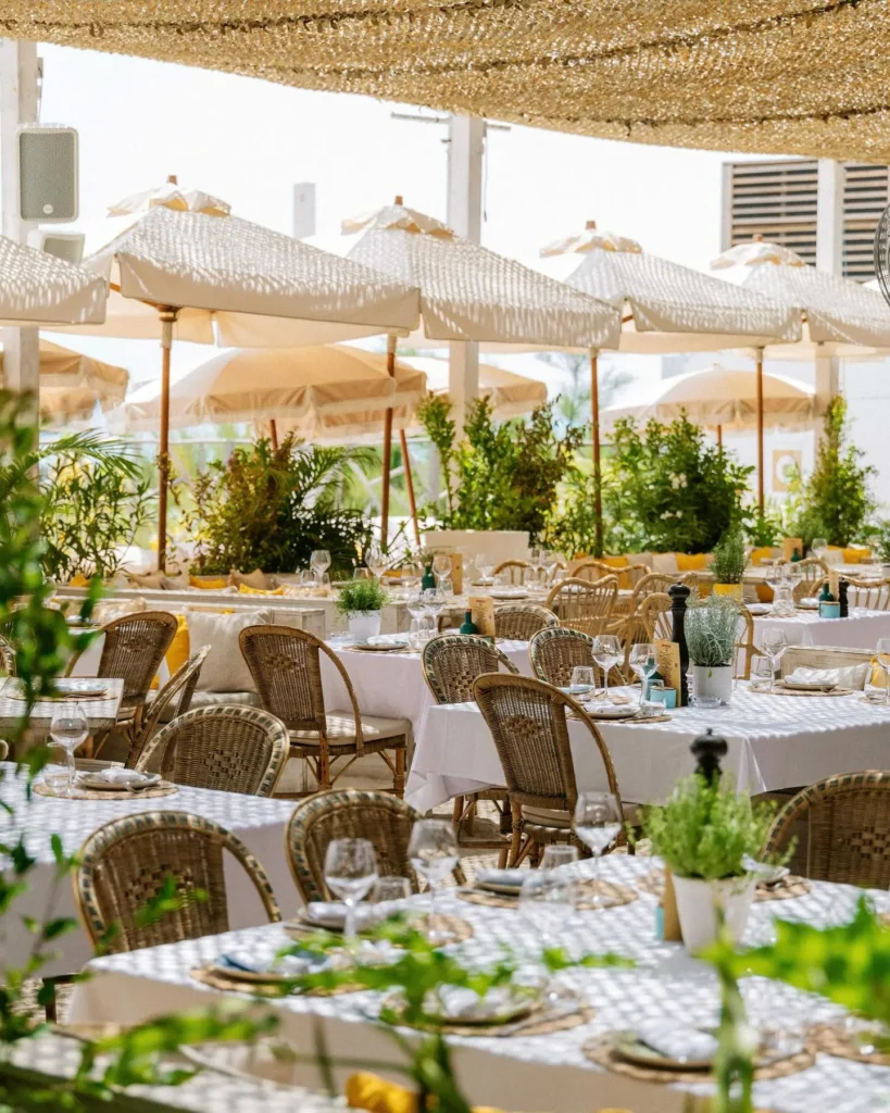 Rattan sofas and pink loungers with a fringed umbrella overlooking the sea at Shellona Saint-Tropez