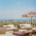 Rattan sofas and pink loungers with a fringed umbrella overlooking the sea at Shellona Saint-Tropez