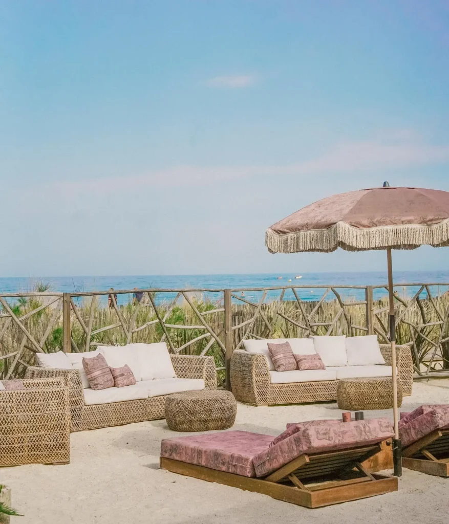 Rattan sofas and pink loungers with a fringed umbrella overlooking the sea at Shellona Saint-Tropez