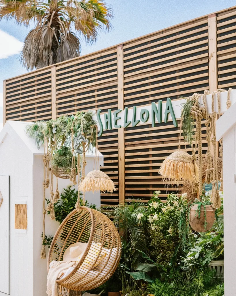 Shellona sign on a slatted wall above a hanging rattan chair and greenery at Shellona Saint-Tropez