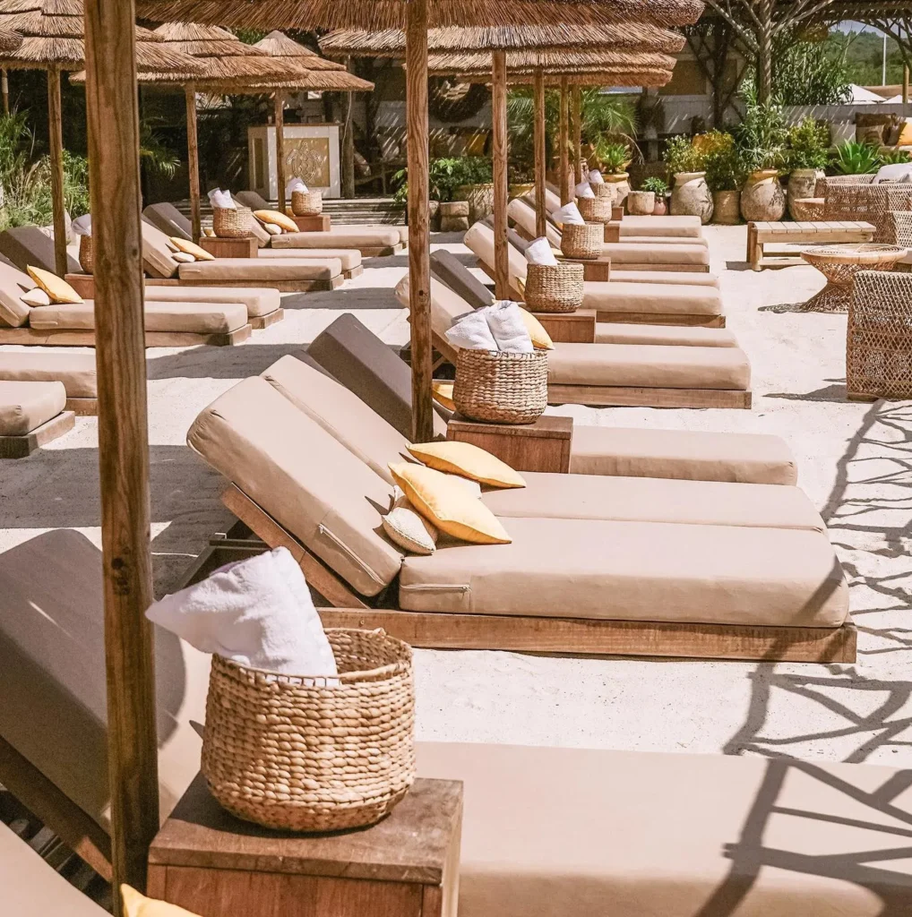 Sunbeds with yellow cushions and woven towel baskets in the sand at Shellona Saint-Tropez