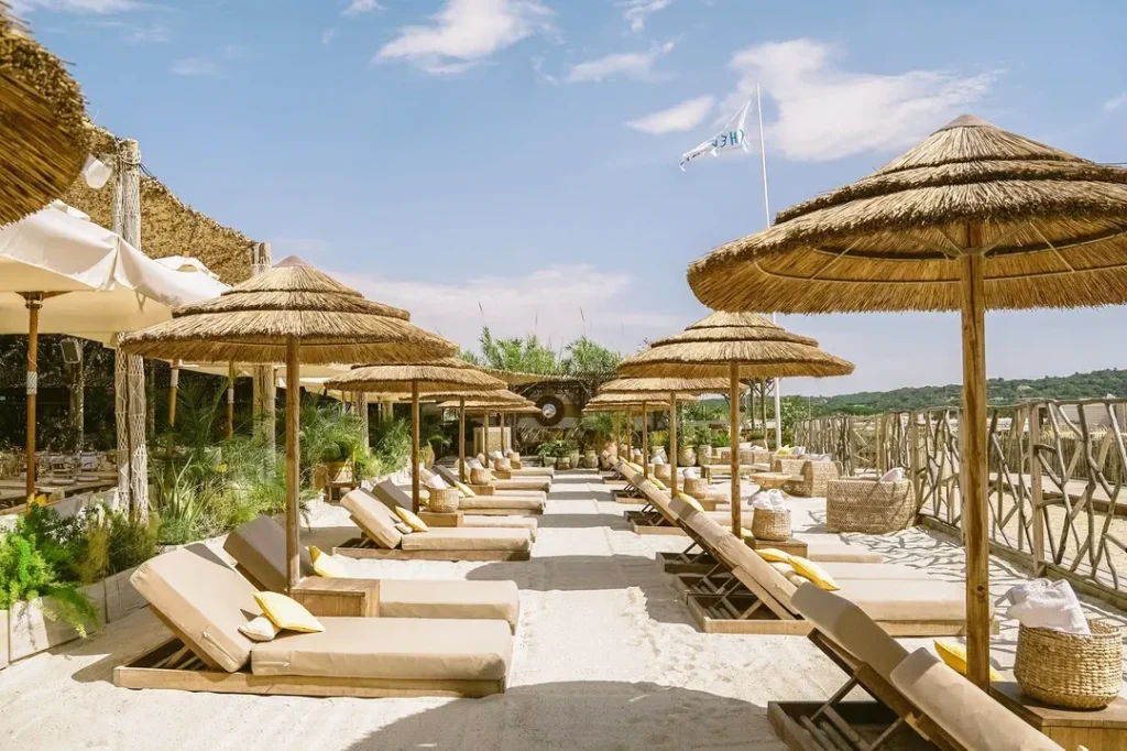 Sandy pathway between sunbeds and thatched umbrellas under the flag at Shellona Saint-Tropez
