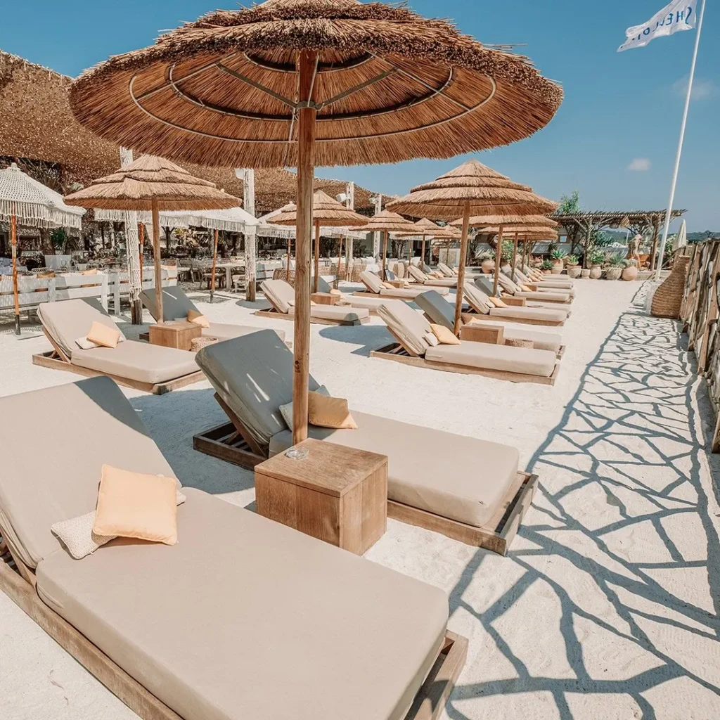 Beige sunbeds under thatched umbrellas on white sand at Shellona Saint-Tropez