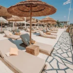 Beige sunbeds under thatched umbrellas on white sand at Shellona Saint-Tropez
