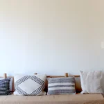 Wooden bench topped with woven and embroidered cushions against a pale wall at SPOT Palma De Mallorca