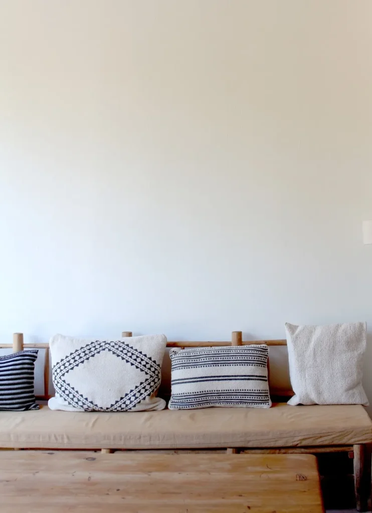 Wooden bench topped with woven and embroidered cushions against a pale wall at SPOT Palma De Mallorca
