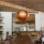 Reclaimed wood communal table under a wooden globe pendant with a large mirror behind at SPOT Palma De Mallorca