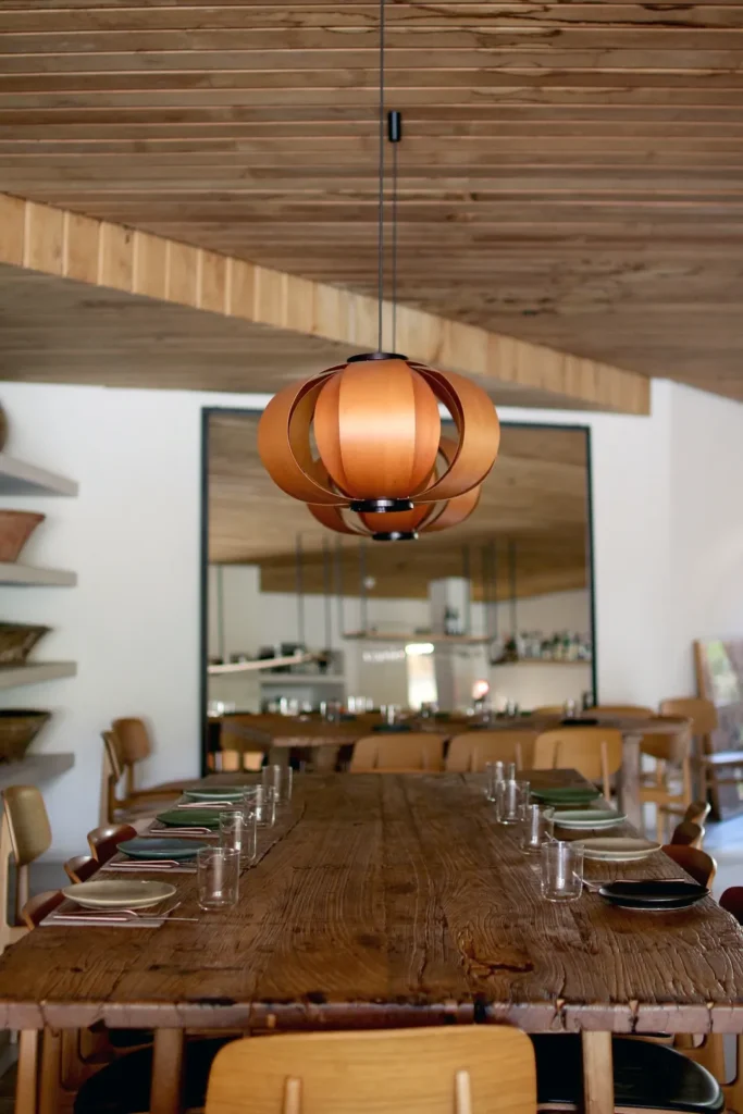 Reclaimed wood communal table under a wooden globe pendant with a large mirror behind at SPOT Palma De Mallorca