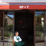 Chef seated laughing in the glass doorway beneath the SPOT sign and red awning at SPOT Palma De Mallorca
