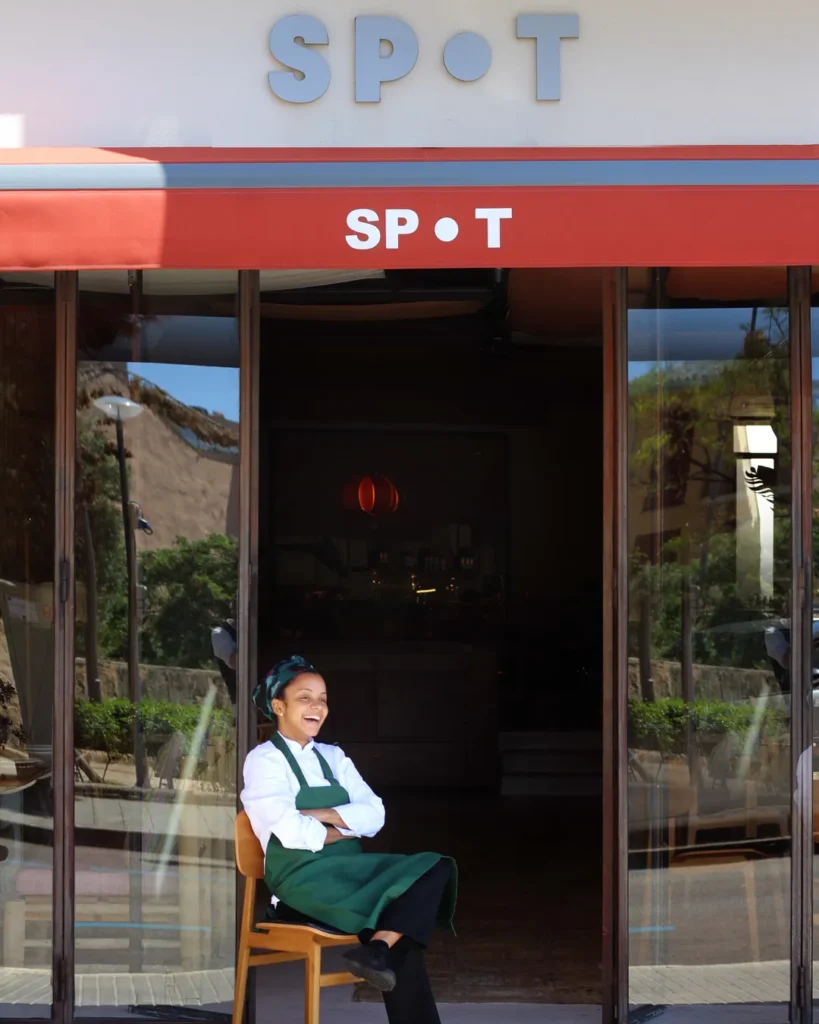 Chef seated laughing in the glass doorway beneath the SPOT sign and red awning at SPOT Palma De Mallorca