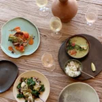Overhead spread of grilled octopus, green curry, salad and wine on a wood table at SPOT Palma De Mallorca