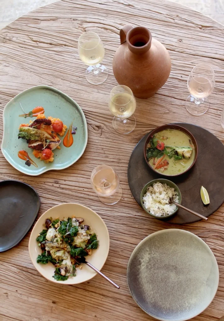 Overhead spread of grilled octopus, green curry, salad and wine on a wood table at SPOT Palma De Mallorca