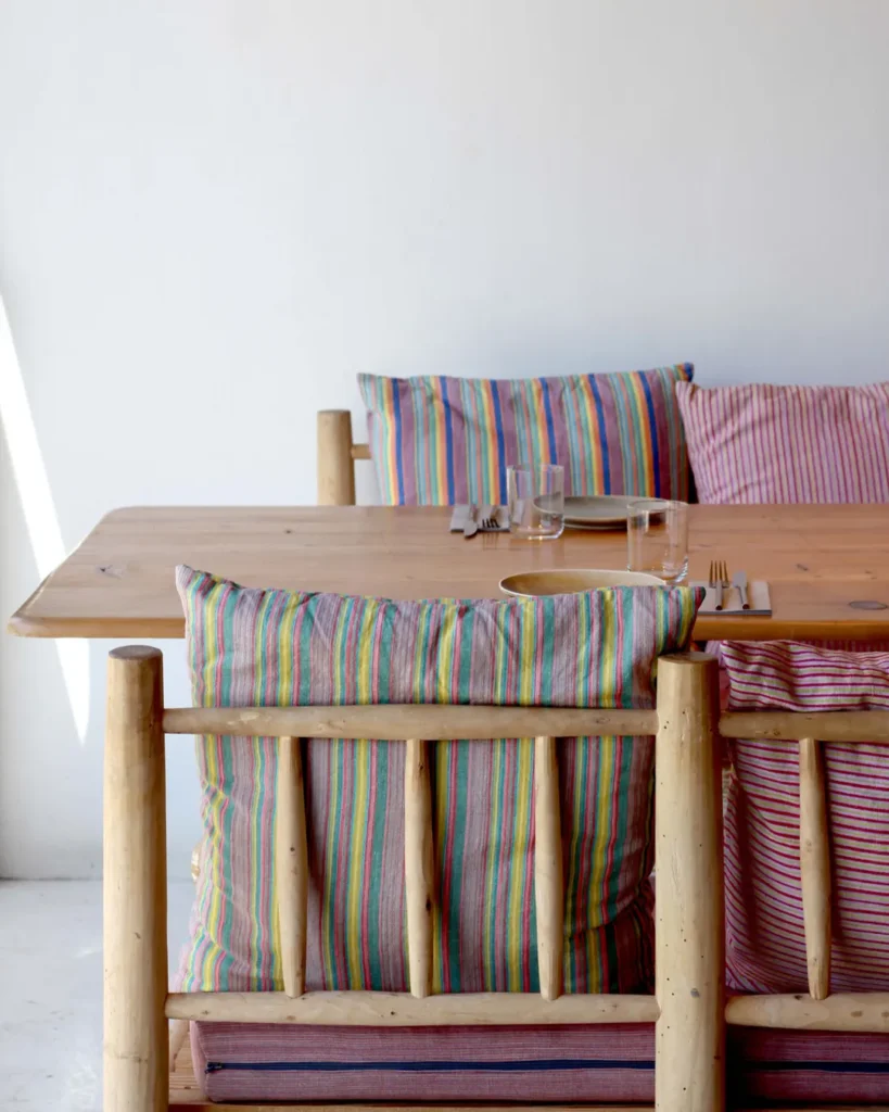 Wooden table and log chairs dressed with rainbow-striped cushions at SPOT Palma De Mallorca