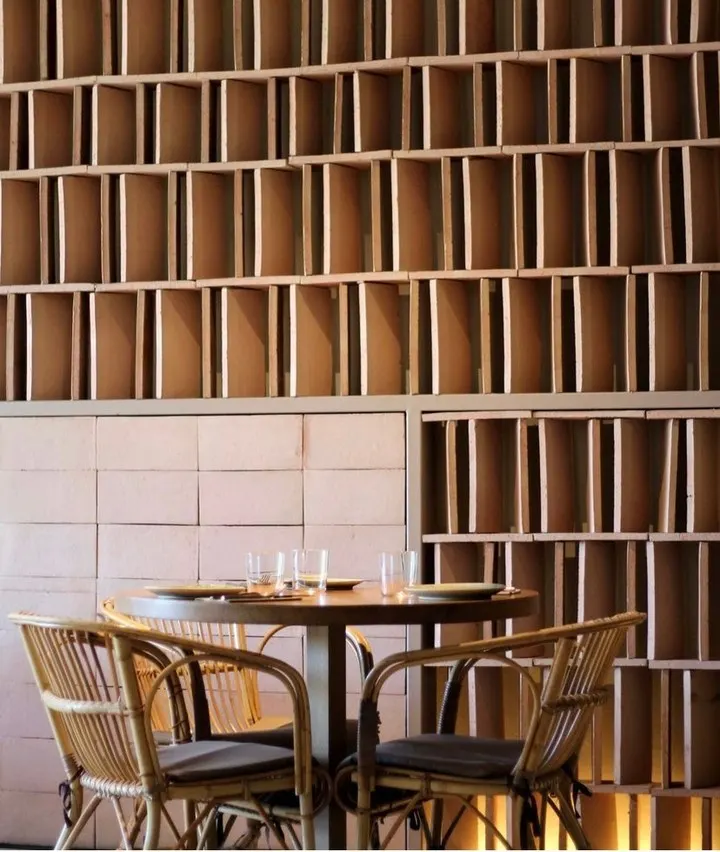 Round table and rattan chairs against a backlit stacked-brick lattice wall at SPOT Palma De Mallorca