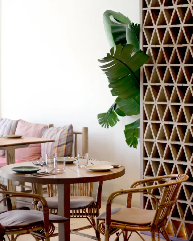 Round table with rattan armchairs beside a breeze-block screen and banana plant at SPOT Palma De Mallorca