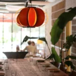 Orange melon pendant lamp over a wood table by the garden windows at SPOT Palma De Mallorca