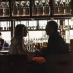 Couple in silhouette talking over drinks at the bar with sake bottles behind at Zuma Cannes