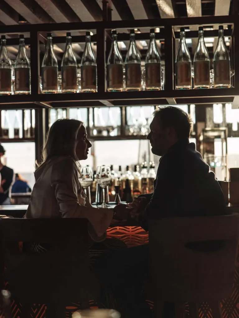 Couple in silhouette talking over drinks at the bar with sake bottles behind at Zuma Cannes