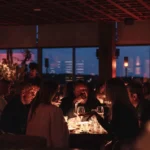 Guests dining by candlelight with city lights through the windows at Zuma Cannes