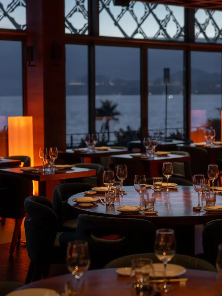 Set tables by full-height windows with a dusk sea view at Zuma Cannes