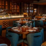 Interior dining room with blue woven chairs and a backlit wine display at Zuma Cannes