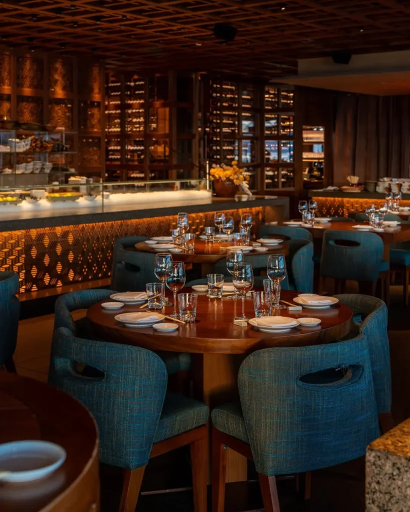 Interior dining room with blue woven chairs and a backlit wine display at Zuma Cannes