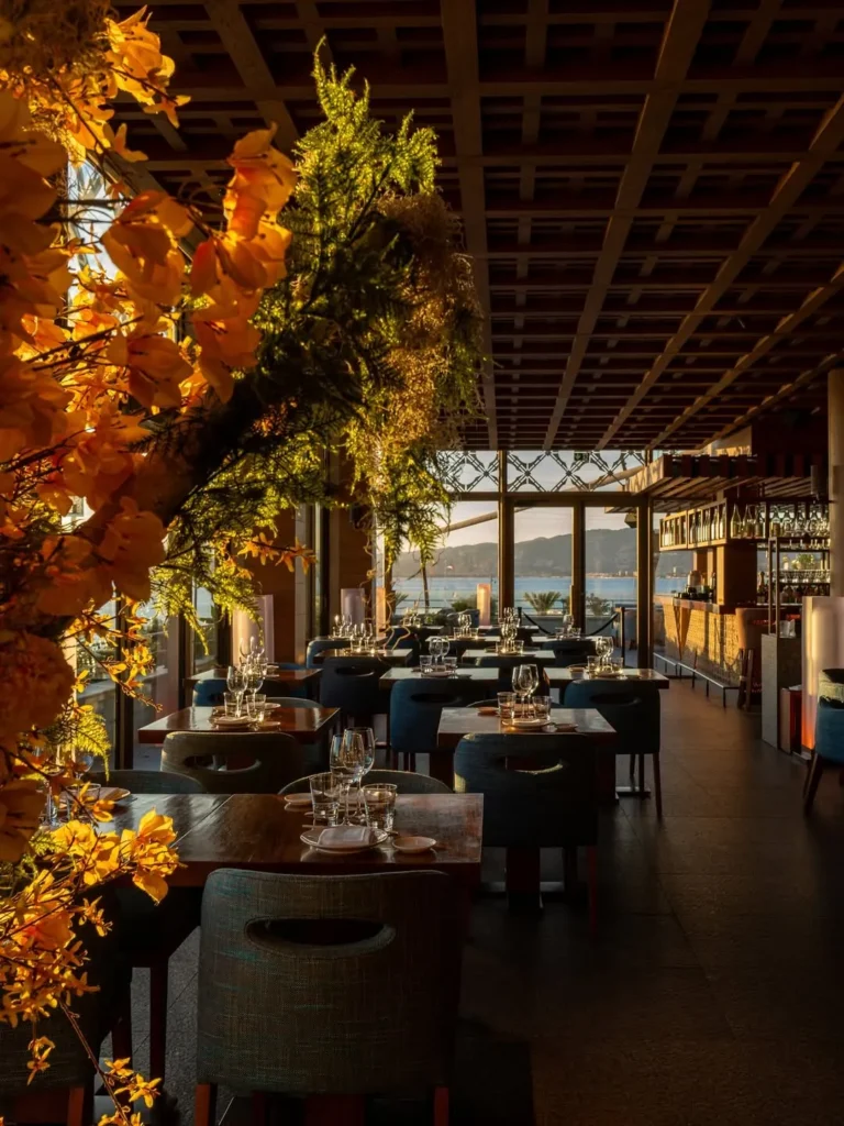 Dining room bathed in sunset light with floral displays and a sea view at Zuma Cannes