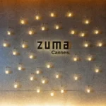 Zuma Cannes logo on a stone wall surrounded by hanging lanterns