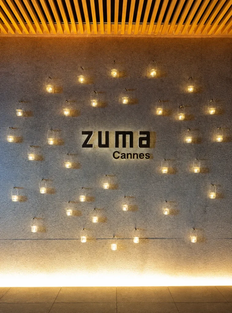 Zuma Cannes logo on a stone wall surrounded by hanging lanterns
